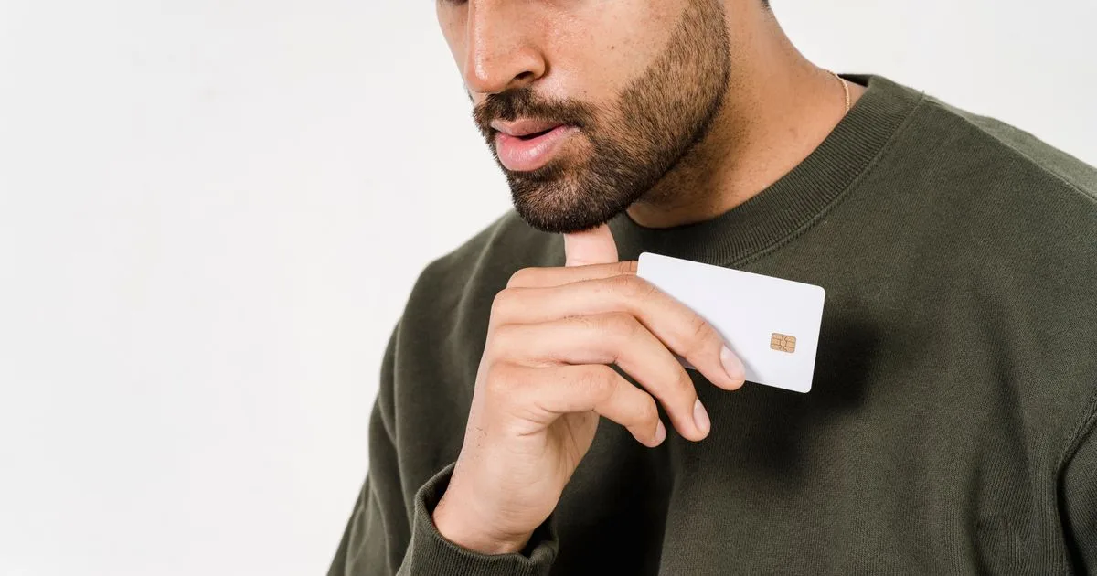 Pensive man weighing credit card advantages and disadvantages while holding a blank card